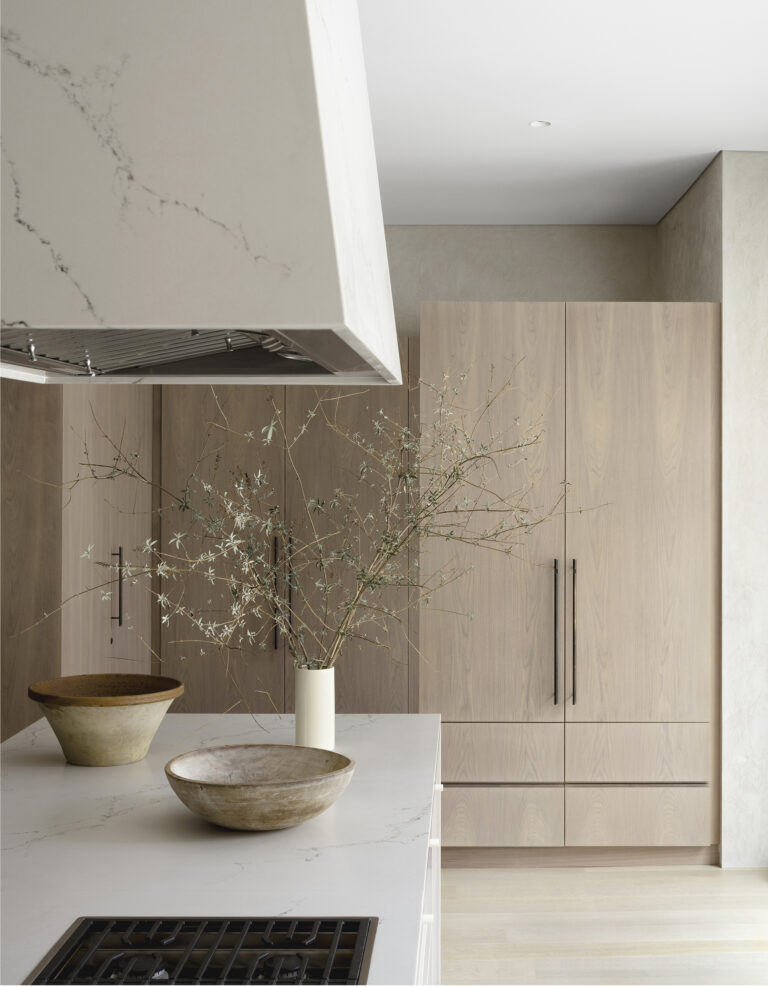 A sculptural, stone-clad hood hangs above the range in an elegant, modern kitchen; custom-finished cabinets and bespoke hardware were designed for the space.