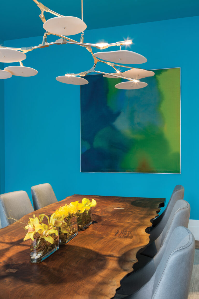 In a dining room, a chandelier by Lindsey Adelman hangs above a live-edge walnut table by bddw and chairs by B&B Italia. Art by Willem de Looper was sourced at Hemphill Gallery.