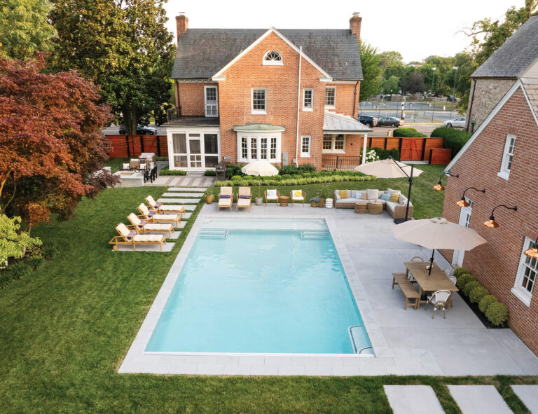 A backyard view reveals an entertainment hub, complete with pool, dining area, grilling station and fire pit; a detached garage borders the pool scape.