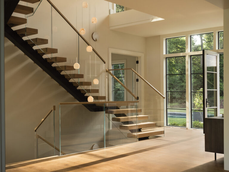 A sculptural, modern stair features white oak treads, a black steel stringer and a glass guardrail.