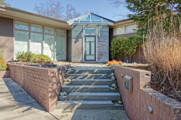A modified entry features new steps and retaining walls leading to a front door integrated into a metal-wrapped box topped by glass.