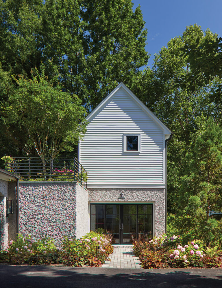 The two-story pool house helps navigate steep grade. The finish combines a stucco foundation with white clapboard siding.