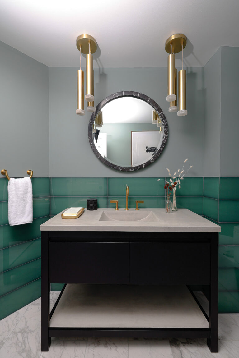 Sculptural brass Arteriors pendants, natural stone and textured, large-format wall tiles elevate a basement bath in Urbana, Maryland.