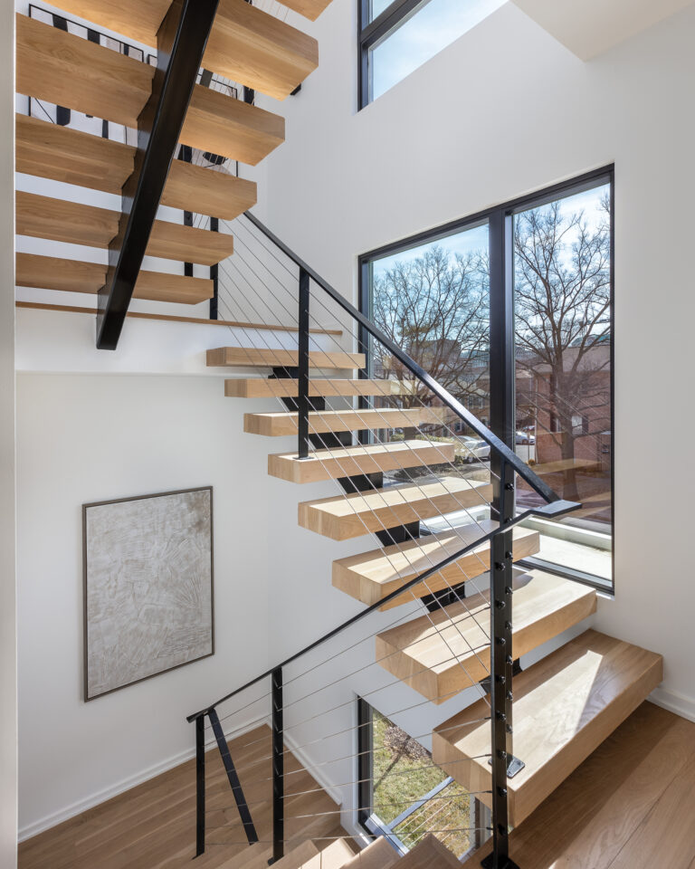 In a modern residence, sunlight washes over a floating staircase that pairs blackened-steel railings with white oak treads.