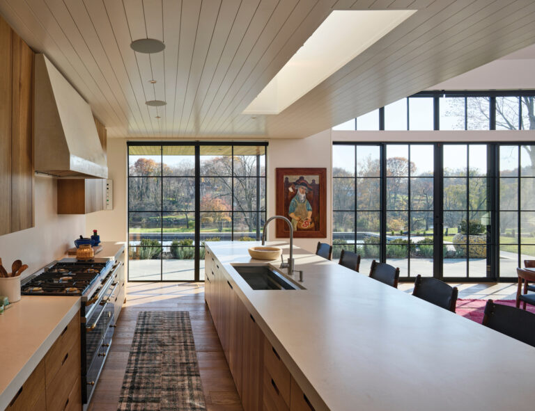 In an open-plan space, the kitchen is defined by a dropped ceiling that contrasts with the adjacent cathedral ceiling. White oak flooring connects the zones.