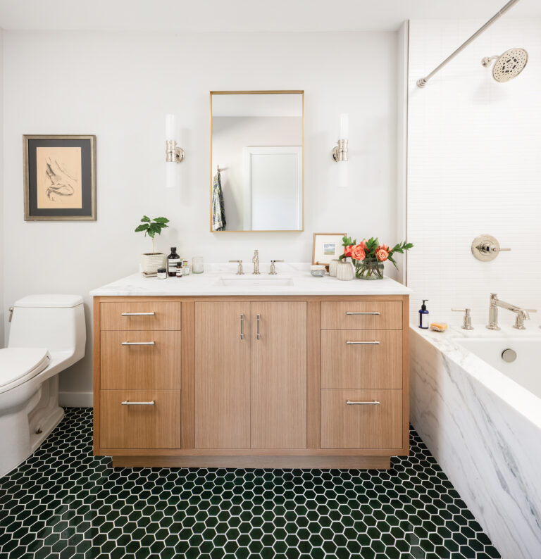 A chic bath features a rift-cut, white oak vanity, with deep green floor tile and dramatic marble tub surround.