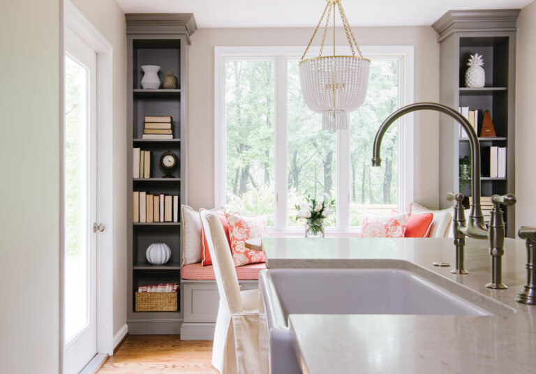 Visible beyond a kitchen island with an apron front sink, built-in bookcases frame a cozy window seat.