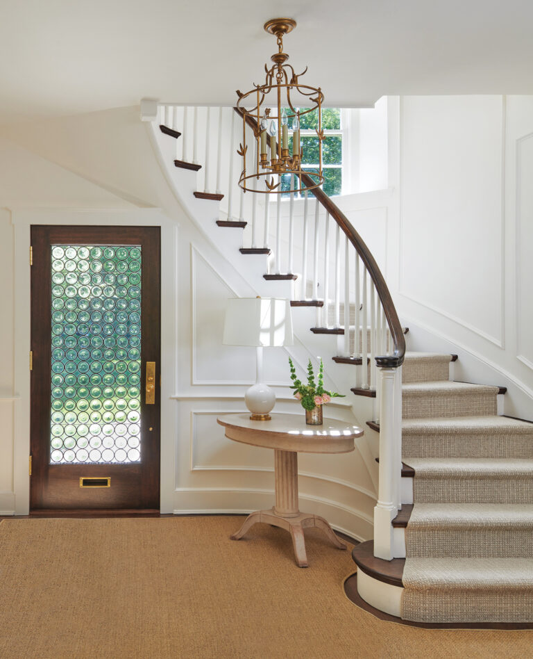 The addition of a bottle-glass front door and millwork on the curved stair imparts elegance to a foyer.