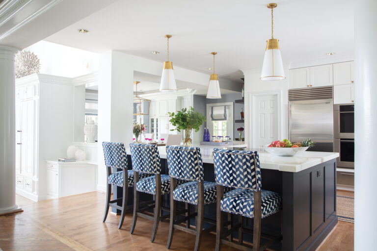 The kitchen in a Lake Anna abode is anchored by an island clad in navy millwork and topped with polished Calacatta Crema Delicato marble.