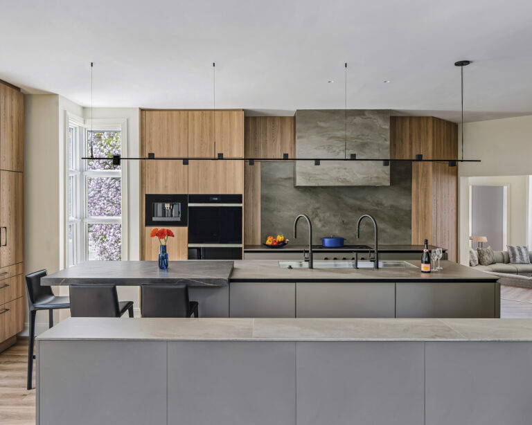 Oak cabinetry and mottled-gray sintered stone surfaces integrate a central island—with dining table and efficient workstation—into a hardworking kitchen.