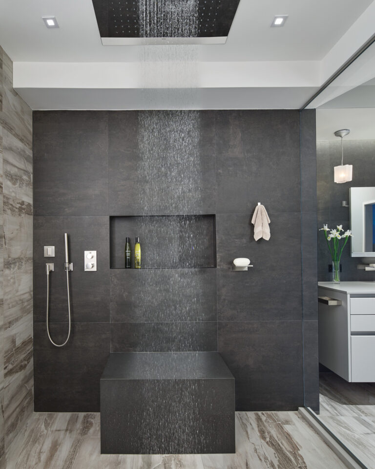 A massive rain shower head, sleek hand shower and chunky custom bench make for this handsome and fully accessible spa shower.