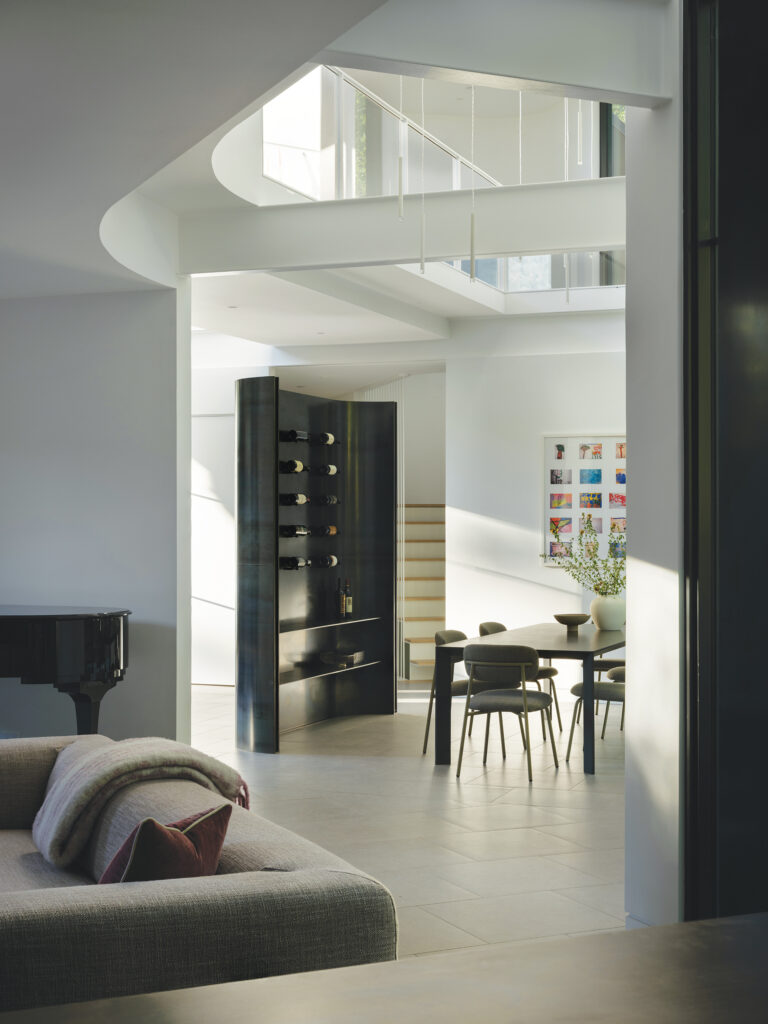 A new, 7,000-square-foot home brings drama via a double-height dining room; a sculpted-steel wine display sits beneath a bridge connecting second-floor zones.