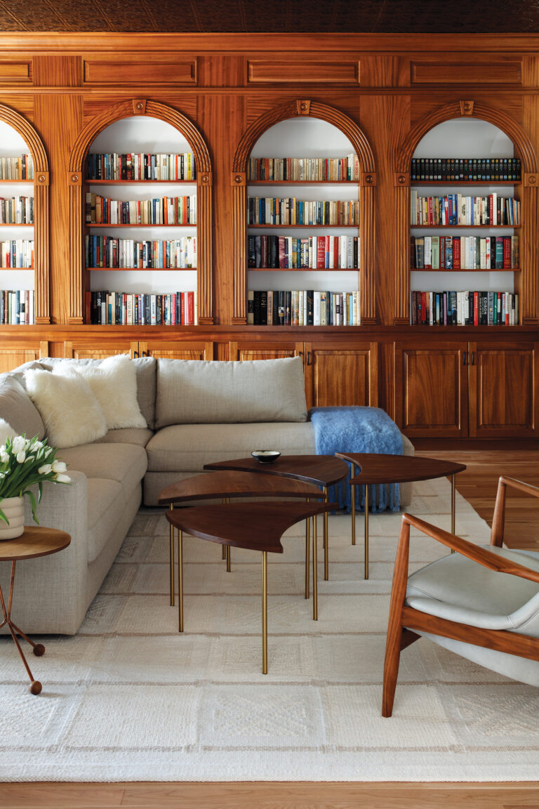 A DWR sofa sits atop a Matt Camron flatweave rug in the den, where eye-catching bookshelves are stained a rich golden hue.