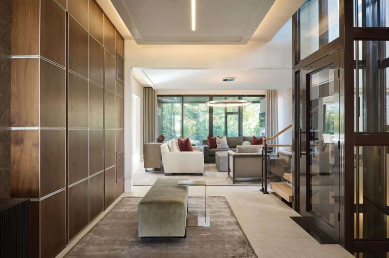 A refined open-concept living space blends warm wood paneling, neutral furnishings and expansive windows that flood the room with natural light.