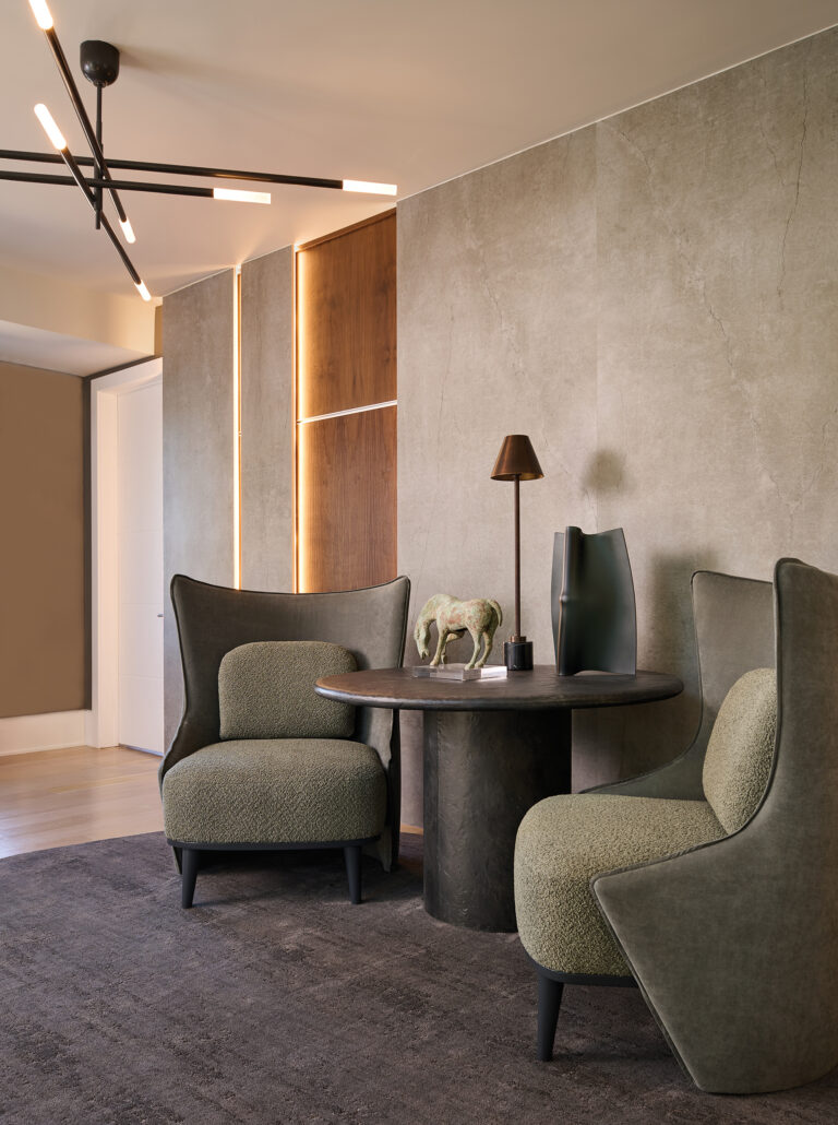 The upper hall features sculptural lounge chairs set against layered porcelain panels and walnut accents, with soft lighting that creates a refined and inviting transition between spaces.