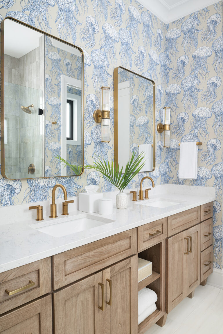 In a Rehoboth Beach, Delaware, getaway, a playful yet polished bathroom pairs whimsical jellyfish wallpaper with warm wood cabinetry and sleek, brass accents.