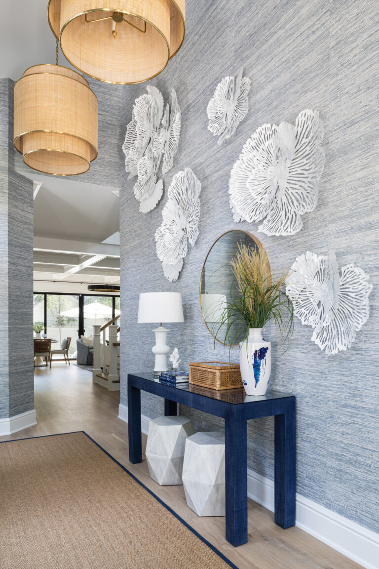 The foyer makes a striking statement with textured, blue grasscloth wallpaper showcasing white, coral-inspired art. A navy console completes the picture.
