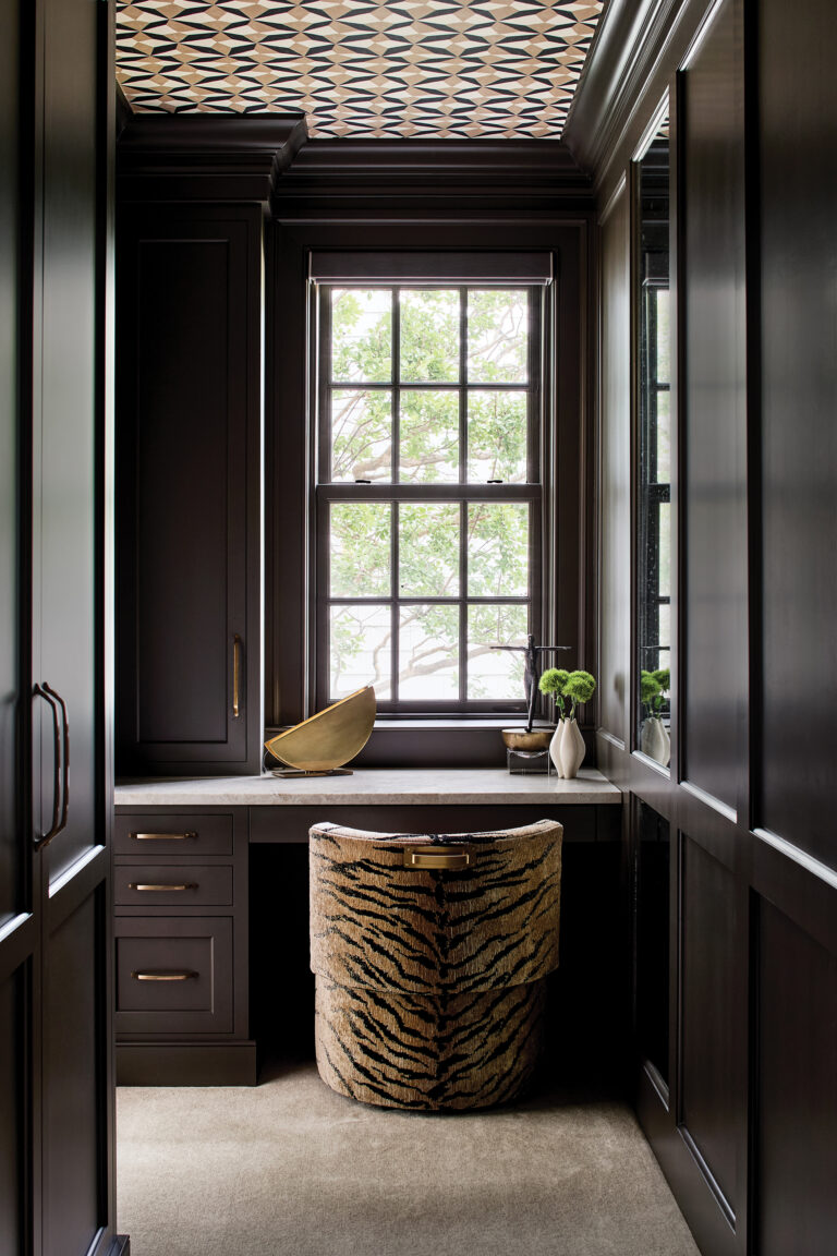 A primary suite in Annapolis boasts a built-in dressing table and millwork finished in Sherwin-Williams’ Urbane Bronze. Striking Romo wallpaper graces the ceiling.