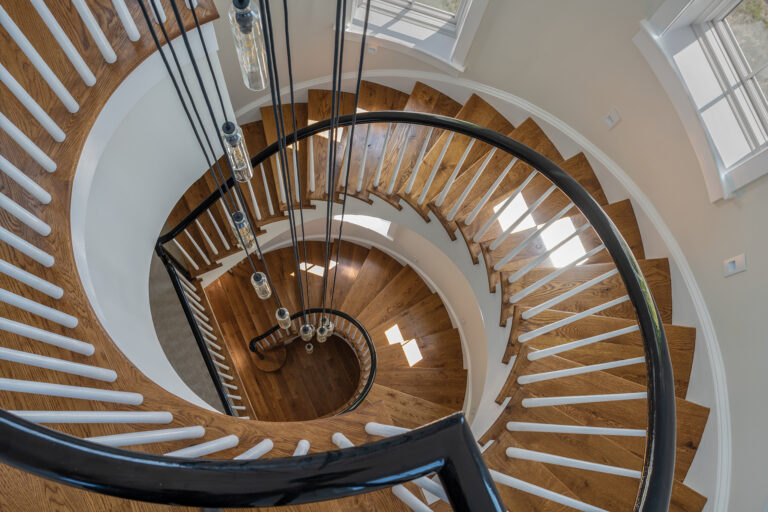 A sweeping spiral staircase pairs warm, wood treads with white spindles and a sleek black rail, creating a striking sculptural moment.