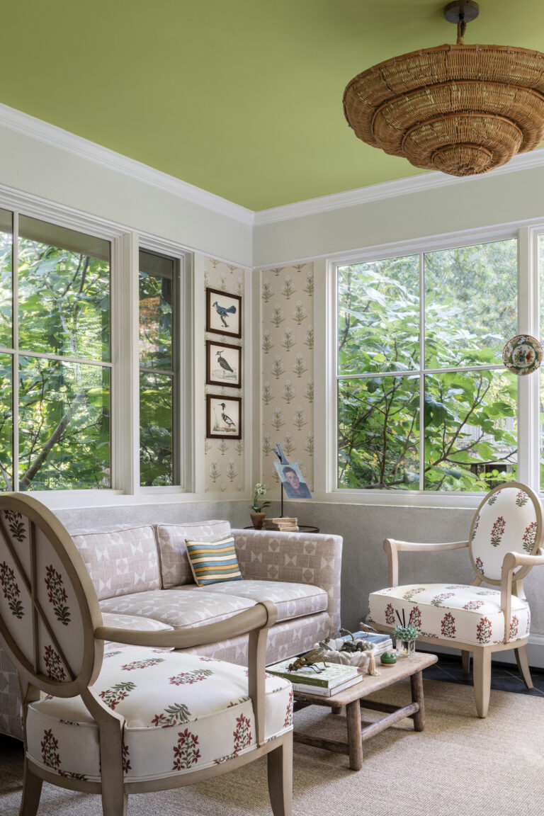 A former screened porch in McLean is now an airy sunroom adorned with a plaster half wall and botanical Casa Branca wallpaper.