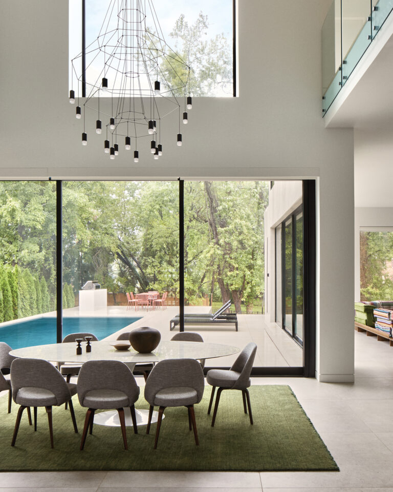 A McLean dining room features a Vibia chandelier above Eero Saarinen furniture. The pool and patio are visible through sliders.