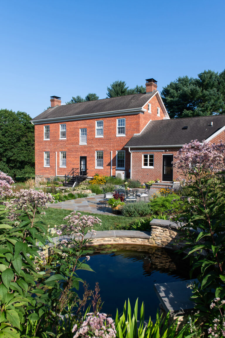 The garden opens gently to the surrounding countryside, where broad skies and rural views shape the experience of being outdoors. The landscape feels seasonal and grounded; an enduring setting where daily life unfolds among flowers, wildlife, and quiet farmland beyond.