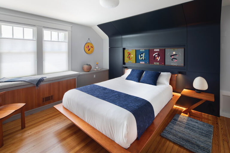 An eye-catching headboard/accent wall follows the line of the attic ceiling in a chic bedroom. A niche integrated into the headboard showcases commissioned Japanese art. 