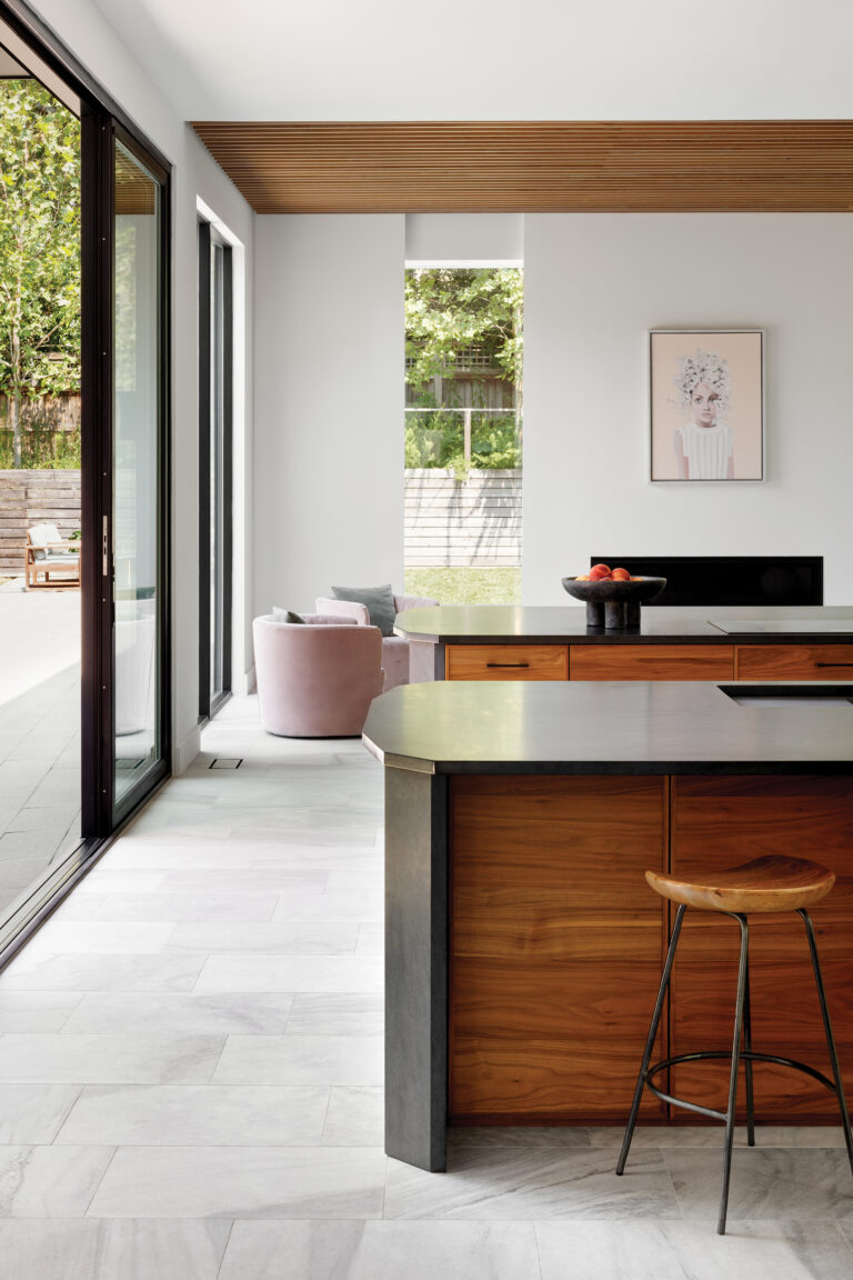 Warm walnut cabinetry and honed-stone countertops anchor a kitchen where expansive glass sliders and a wood-slat ceiling blur the line between indoors and out.