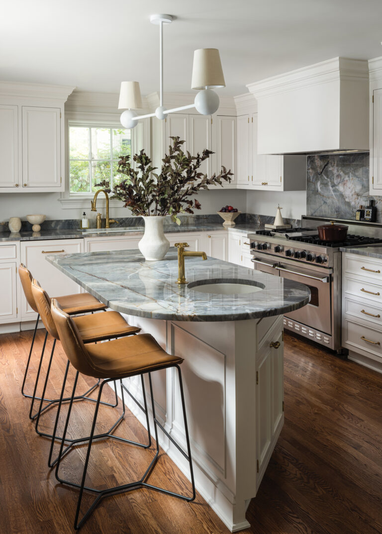 A refresh transformed a kitchen without touching the cabinet boxes—quartzite countertops, a stone-slab backsplash and a sculptural chandelier did the work. 