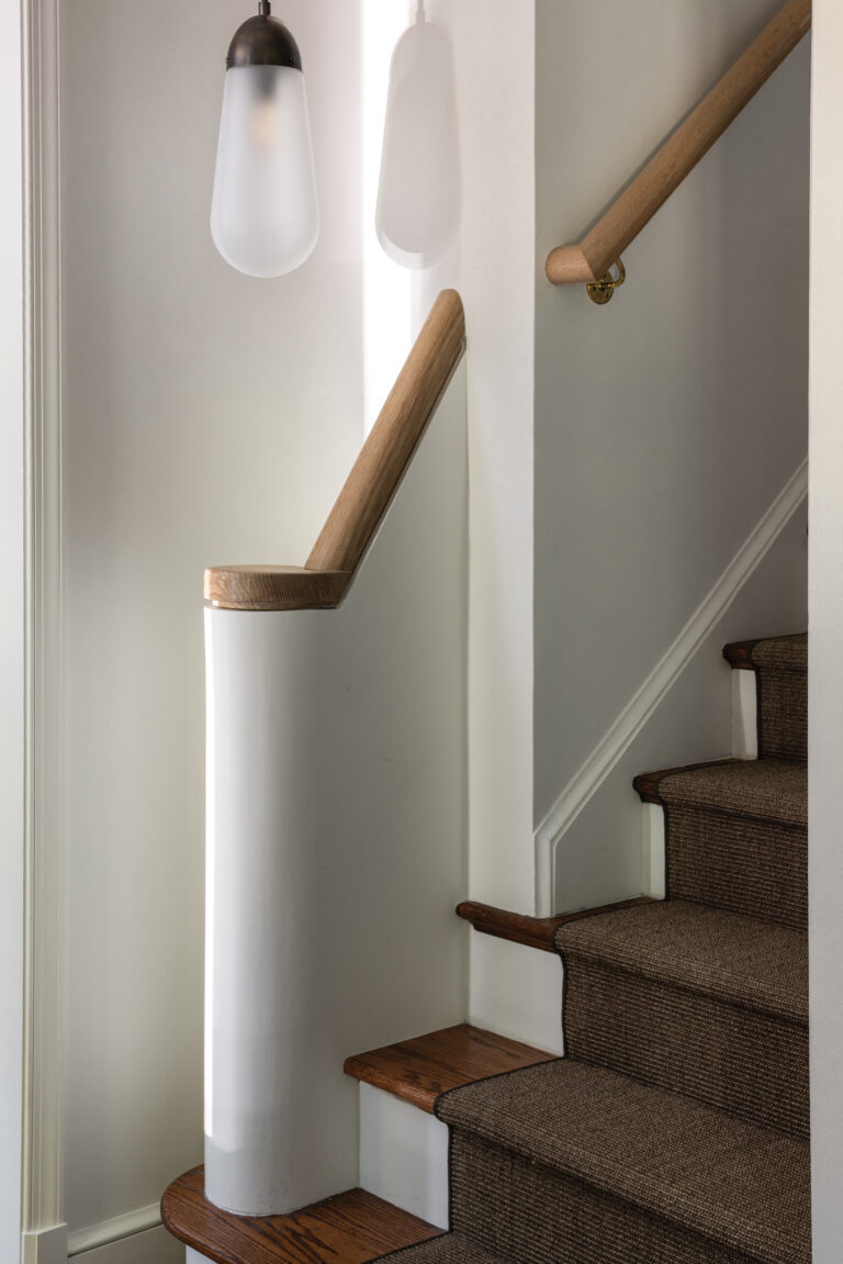 A rounded plaster newel post and white oak handrail impart architectural presence to a stair hall. 