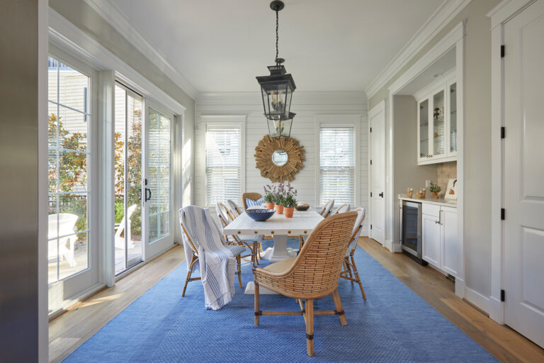 The airy breakfast room in a beach house centers on a sculptural wood sunburst mirror; woven Lexington end chairs create a visual connection.